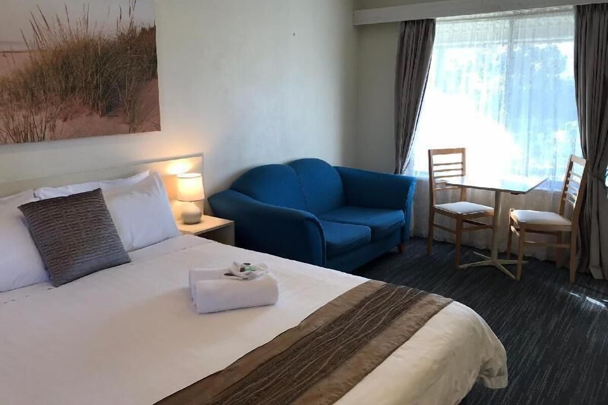 A hotel room with a bed, a blue sofa, a small table with chairs, and a painting on the wall.