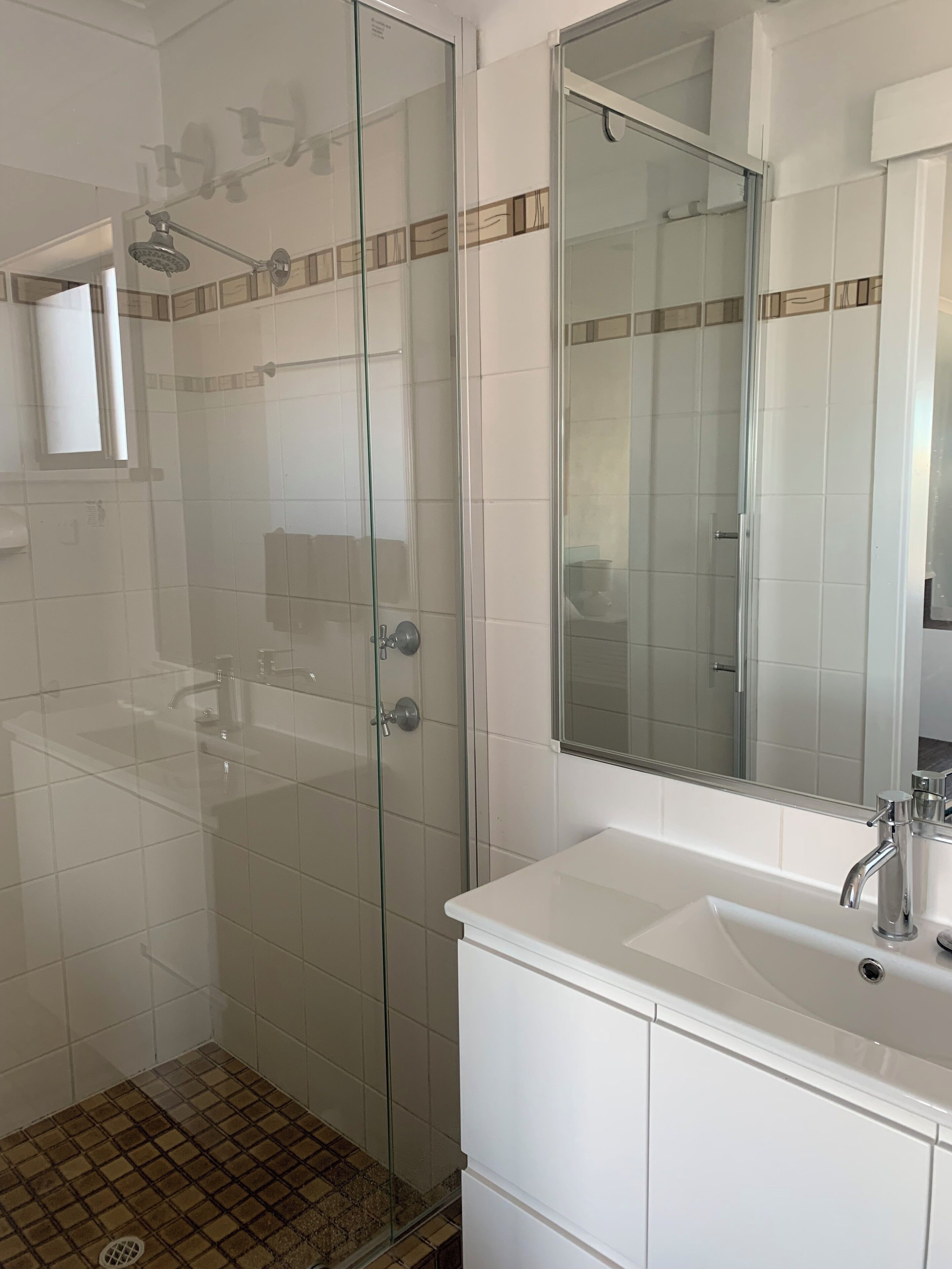 A modern bathroom with a glass-enclosed shower, a white sink, and a large mirror.