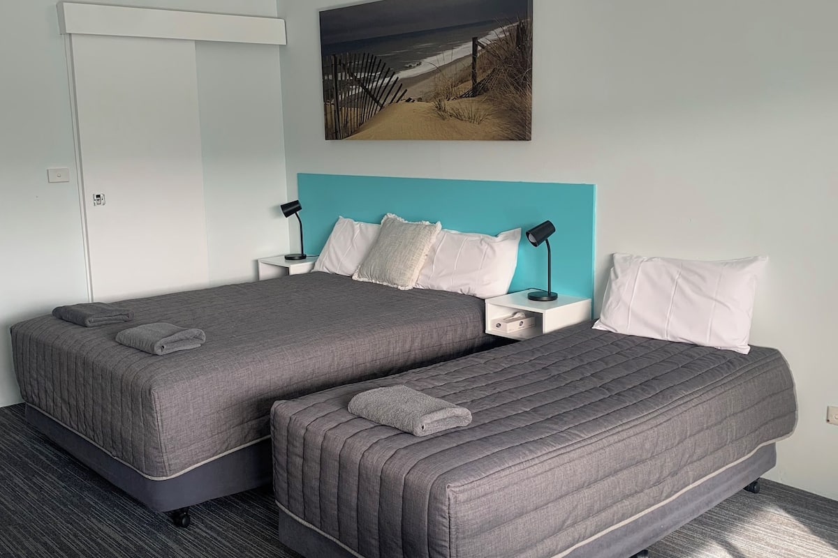 A hotel room with two beds, a view of the beach, and a white door.