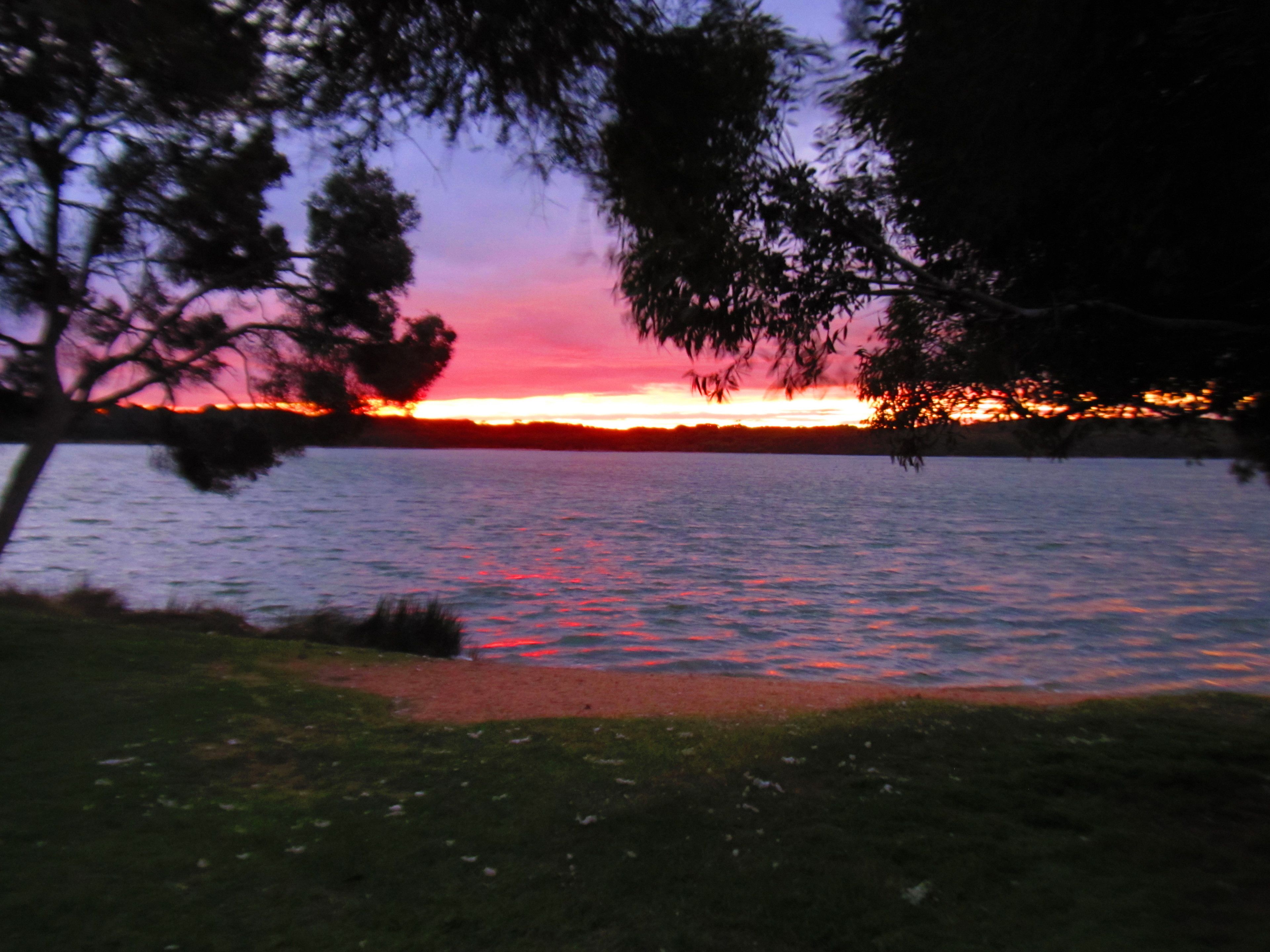 A sunset over a calm lake with trees in the foreground.