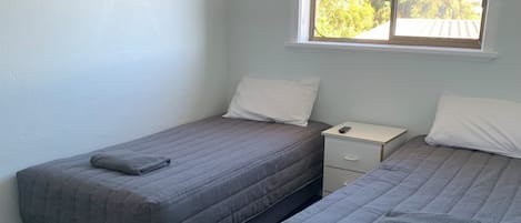 A room with two beds, a window with a view of trees, and a painting on the wall.