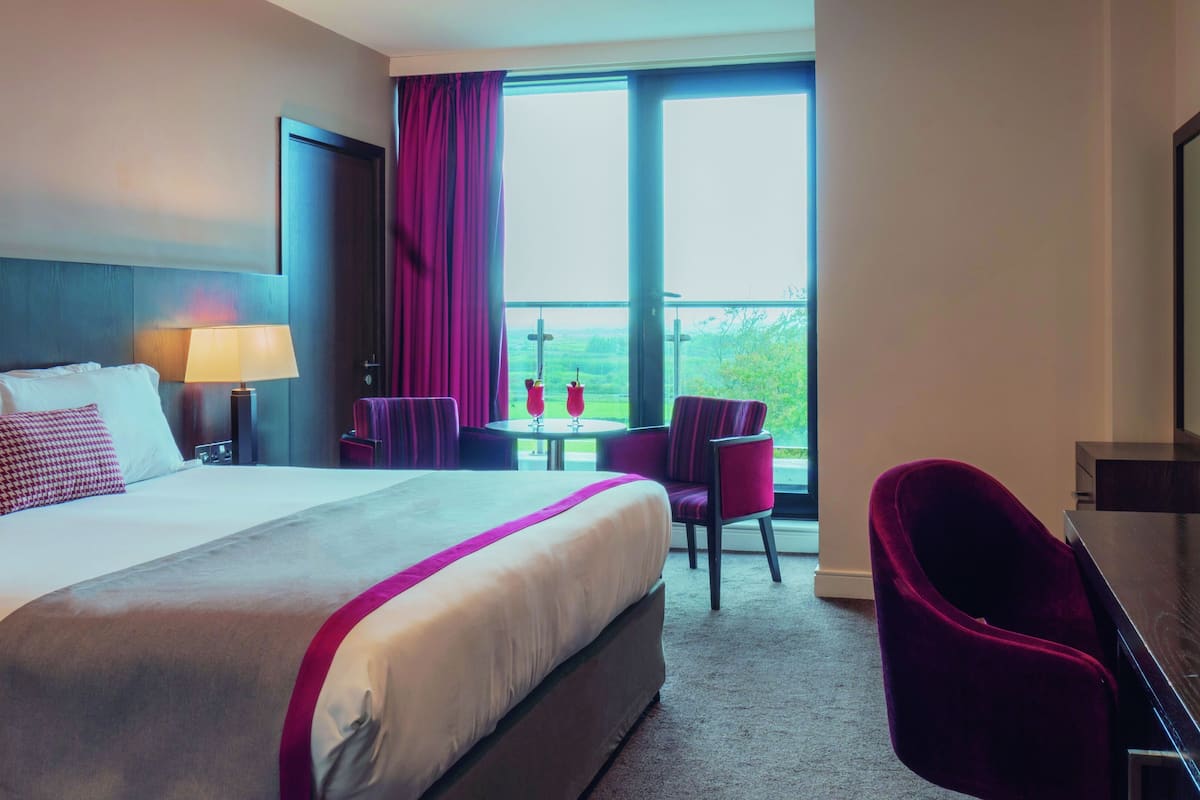 A hotel room with a large bed, a desk, a chair, and a view of the outdoors.