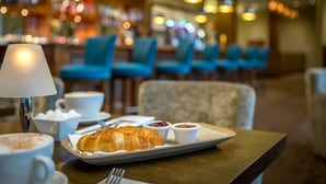 A dining table with a croissant, coffee, and condiments.