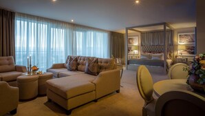 A spacious living room with a sofa, ottoman, and a dining area with a chair. There is a bedroom with a bed and a nightstand.