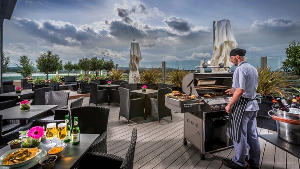 An outdoor dining area with wicker furniture, a grill station, and a view of the ocean.