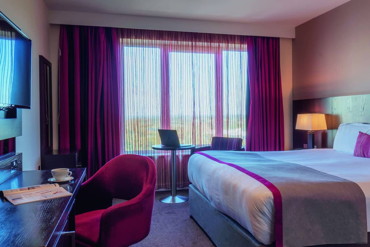 A hotel room with a large bed, a desk with a laptop, a chair, and a TV.