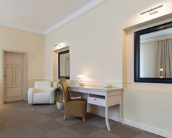 Una camera d'albergo con una scrivania bianca, una sedia, una pianta in vaso e un grande specchio.