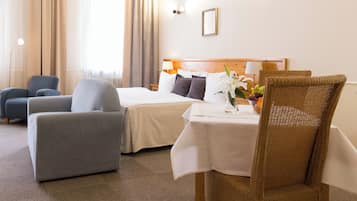 Un cuarto de hotel con una cama, dos sillones, una mesa de comedor con un jarrón de flores y vistas al exterior.