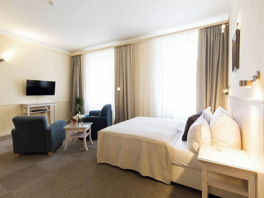 Une chambre d’hôtel avec un lit, un bureau, une chaise, une télévision et une fenêtre avec des rideaux.
