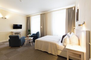 A hotel room with a bed, a desk, a chair, a TV, and a window with curtains.