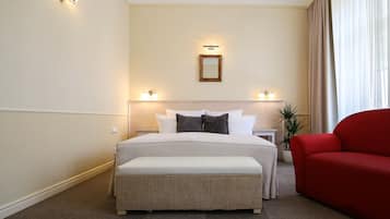 A hotel room with a large bed, two bedside tables, a red armchair, and a potted plant.
