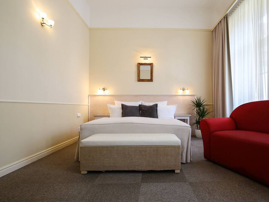 A hotel room with a large bed, two bedside tables, a red armchair, and a potted plant.