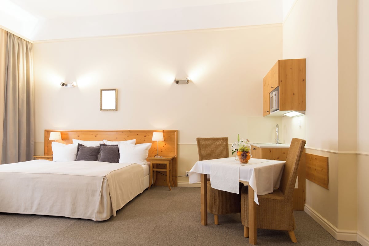 Hotellihuone, jossa on kaksi sänkyä, pieni pöytä, jossa on maljakko täynnä kukkia, tuoli ja puinen kaappi.