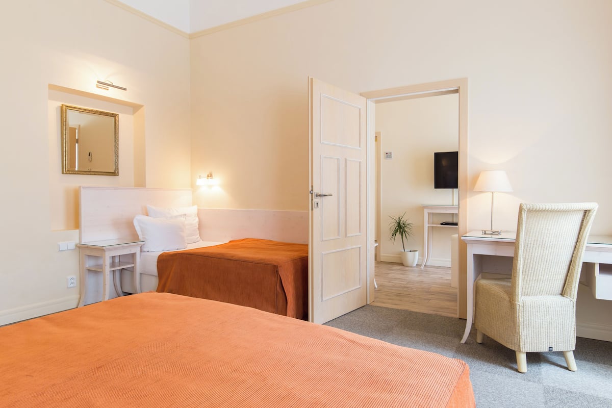 Hotellihuone, jossa on sänky, työpöytä, tuoli, televisio ja pieni pöytä, jossa on lamppu.