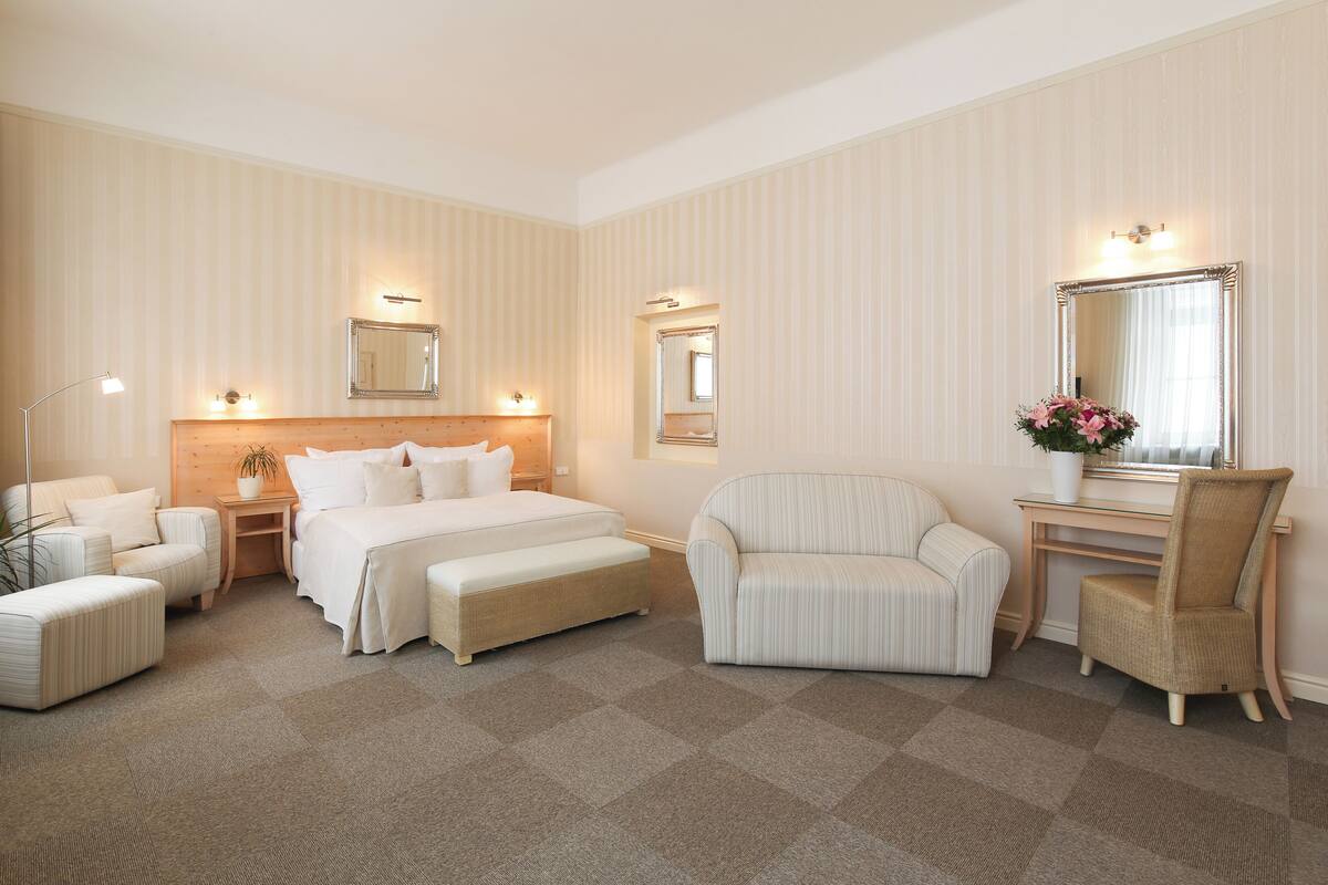 Hotellihuone, jossa on suuri sänky, kaksi yöpöytää, tuoli, työpöytä ja peili.