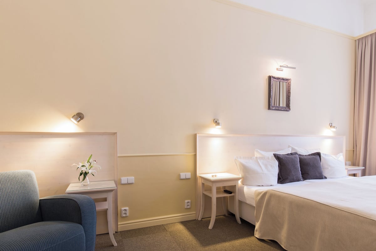 Hotellihuone, jossa on sänky, tuoli, yöpöytä ja seinään kiinnitetty valaisin.