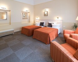 Quarto de hotel com duas camas, um banco e um sofá.