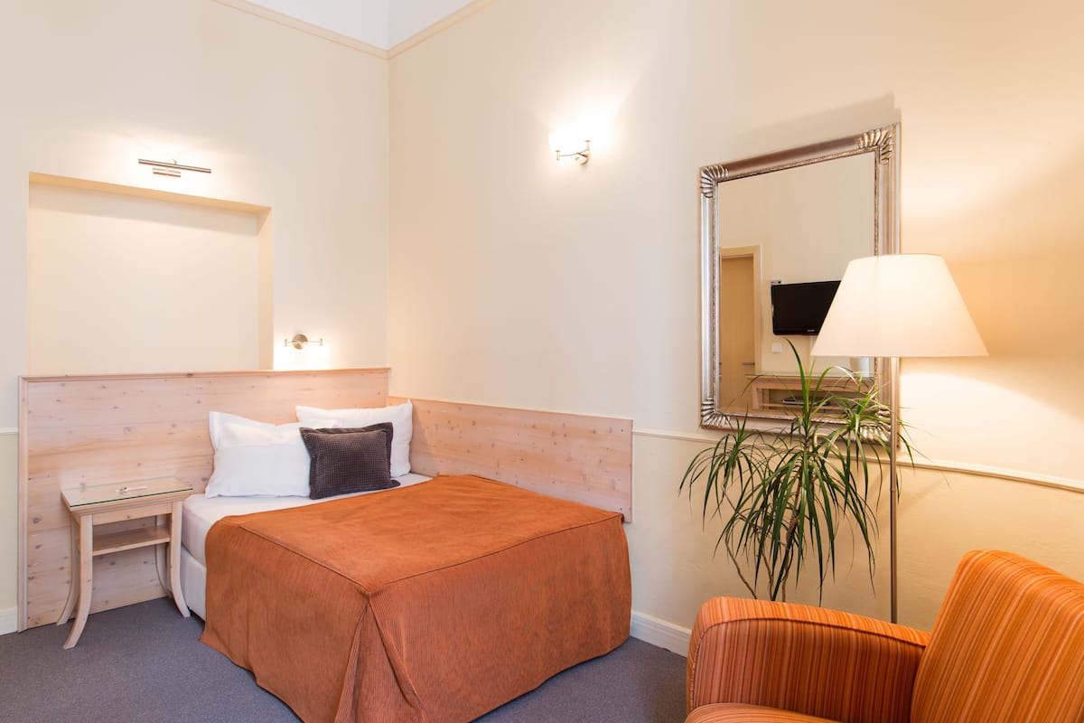 Hotellihuone, jossa on sänky, yöpöytä, tuoli, peili ja lamppu.