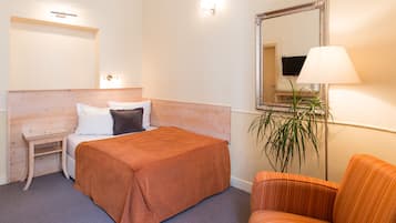 Quarto de hotel com cama, mesa de cabeceira, uma cadeira, um espelho e uma luminária.