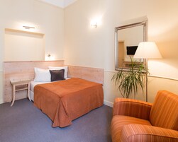 Quarto de hotel com cama, mesa de cabeceira, uma cadeira, um espelho e uma luminária.