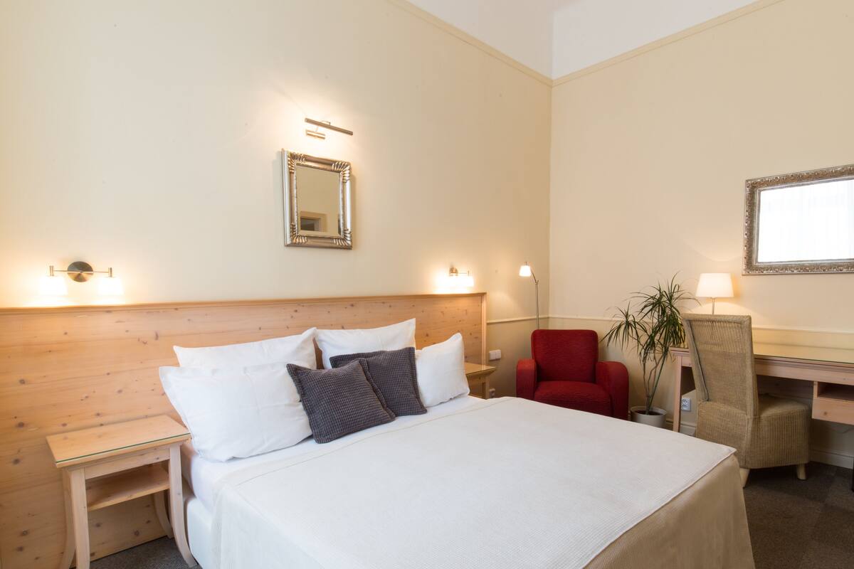 Hotellihuone, jossa on suuri sänky, työpöytä, tuoli ja ruukussa oleva kasvi.