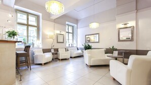 Un vestíbulo amplio con sofás de cuero blanco, un mostrador de recepción y ventanas grandes que dejan entrar luz natural.