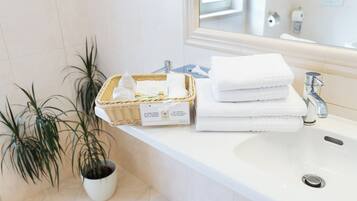 A bathroom with a white sink, a mirror, a wicker basket with toiletries, and two potted plants.
