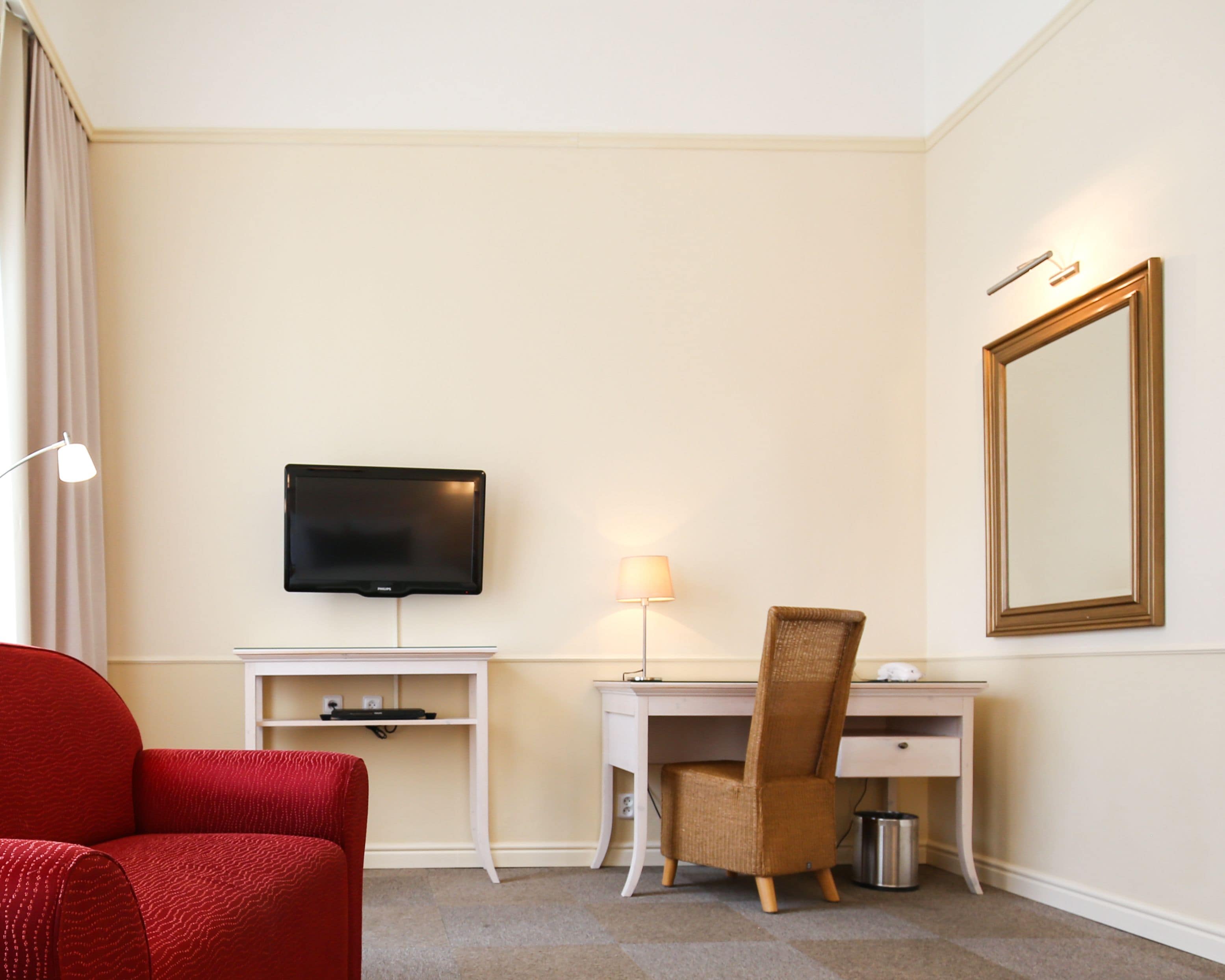 Une chambre d’hôtel équipée d’un téléviseur fixé au mur, d’un bureau avec une lampe, d’une chaise et d’un grand miroir.