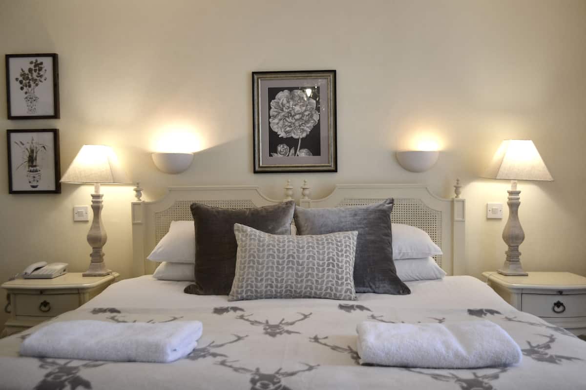 A neatly made bed with a floral bedspread, two wall-mounted lamps, and framed artwork on the wall.