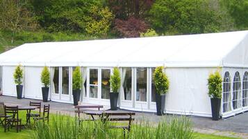 A large white tent with multiple windows and doors, surrounded by outdoor seating and potted plants.
