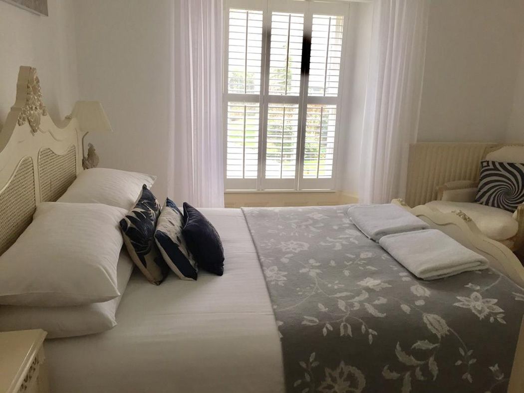 Una cama bien hecha con colcha floral, una lámpara de noche y una silla con cojín estampado.
