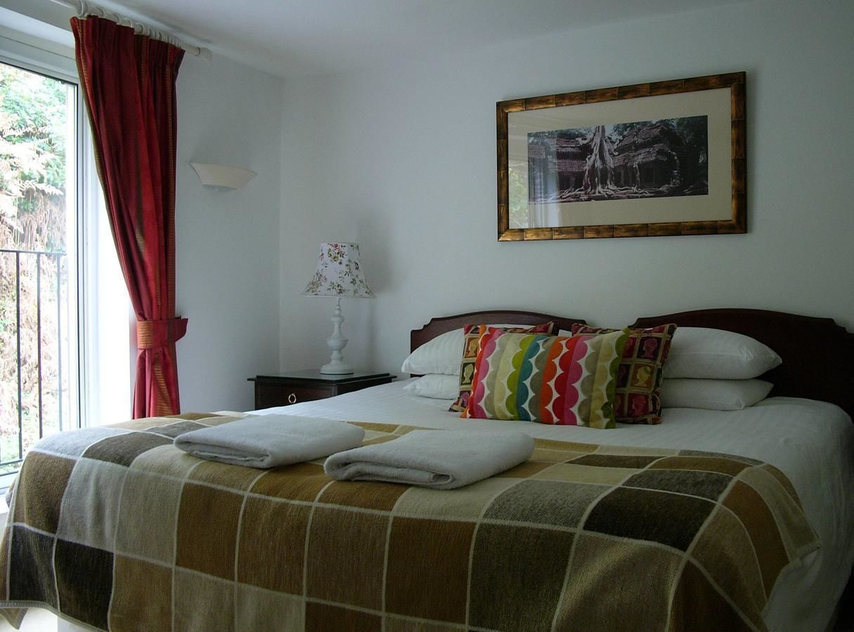 A neatly made bed with a checkered bedspread, a colorful pillow, and two folded towels.
