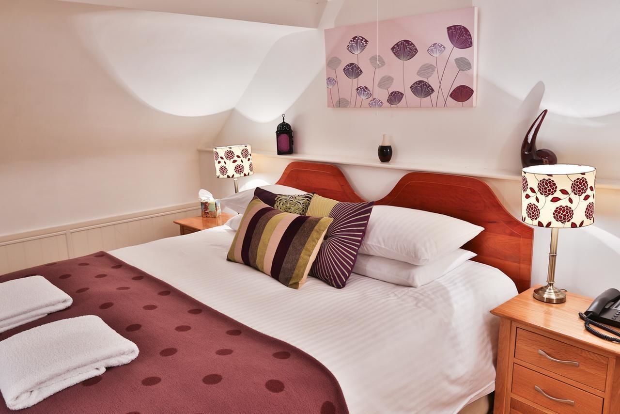 Una habitación de hotel con una cama bien hecha, un cabecero rojo, una obra de arte colgada en la pared, una lámpara de noche y una mesita de noche con un teléfono.