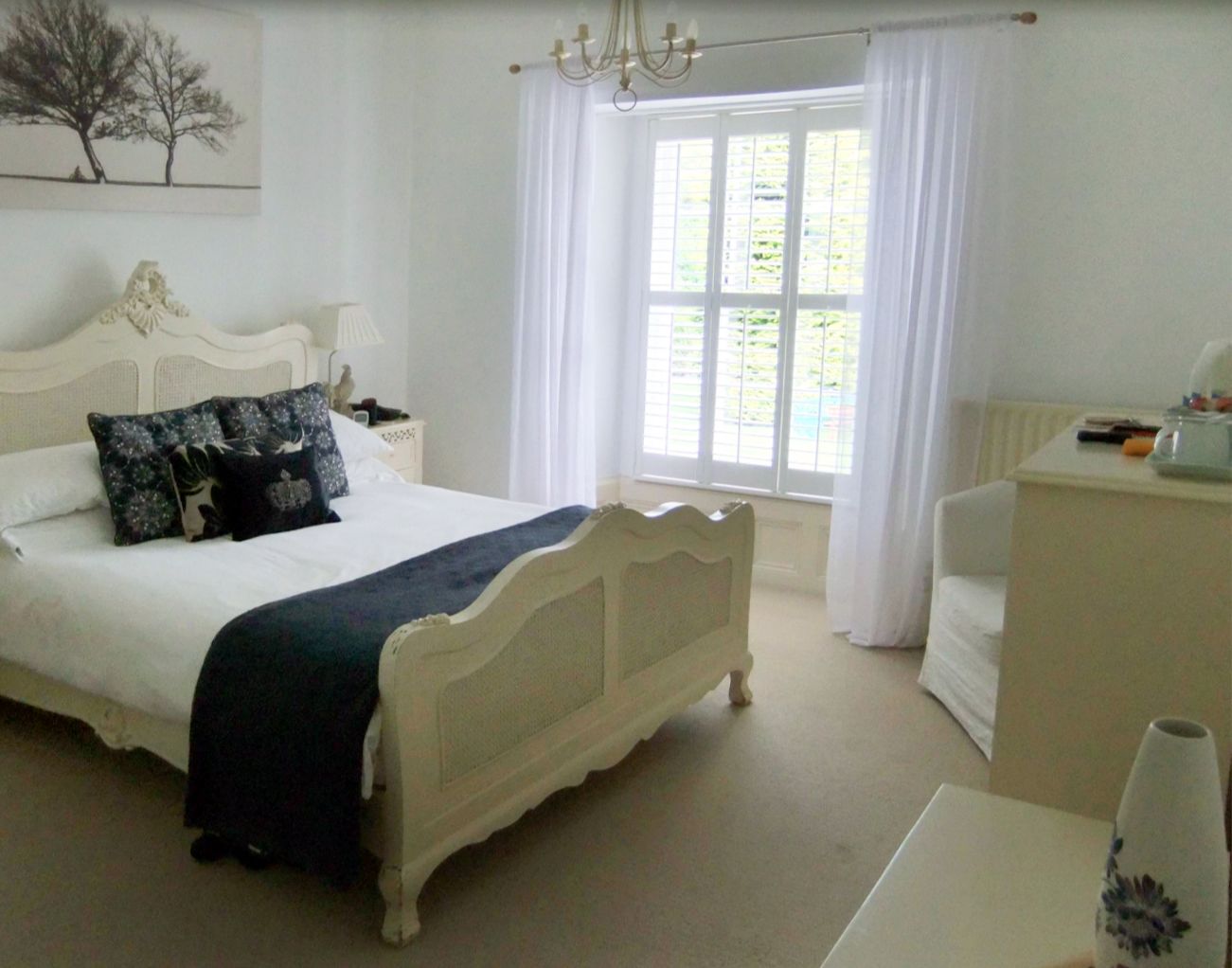 A bedroom with a bed, a nightstand, a dresser, a window with curtains, and a chandelier.
