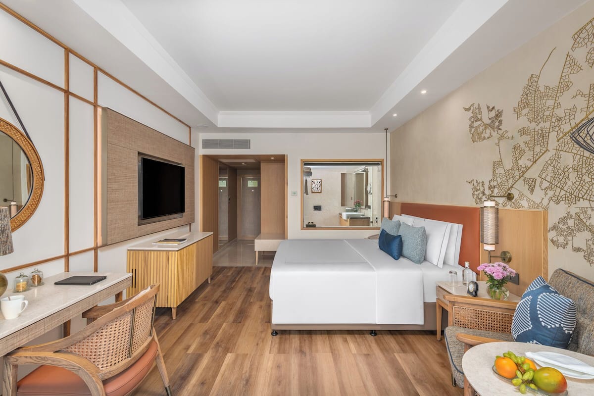 Habitación de hotel con cama, escritorio, televisor, espejo y una pared con diseño decorativo.