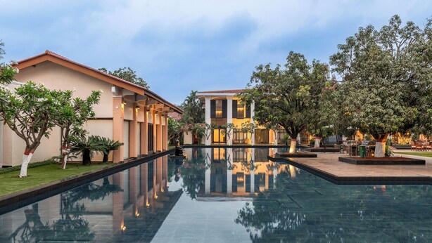 A pool area with a reflection of a building and trees, surrounded by well-maintained grass and a clear sky. - Taj Alibaug Resort & Spa (Alibag)