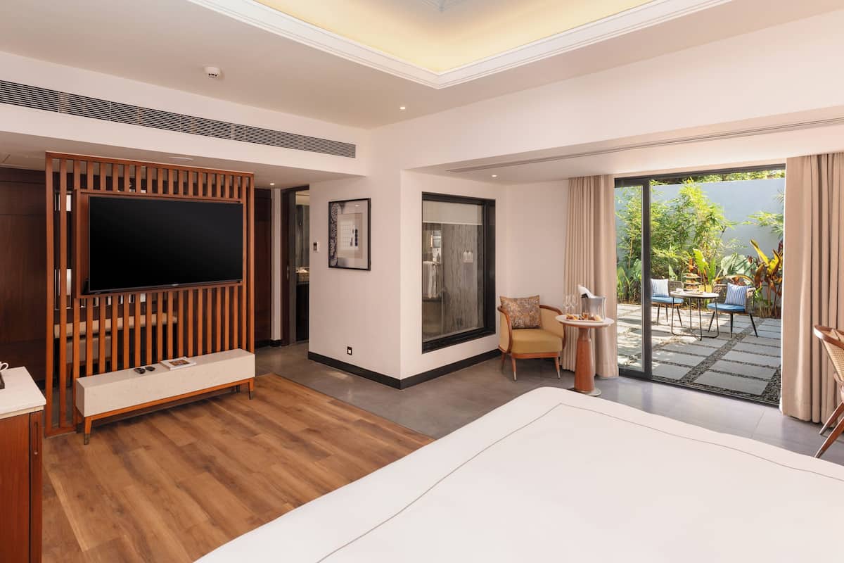 Un hotel moderno con televisor, muebles de madera, una pequeña mesa, un sofá y vistas al jardín exterior.