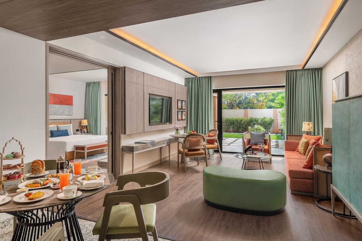 Una habitación de hotel moderna con zona de comedor, sofá, televisión y balcón.
