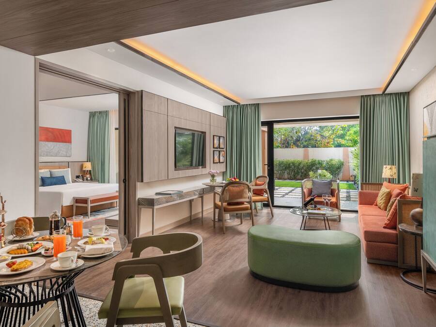 Una habitación de hotel moderna con zona de comedor, sofá, televisión y balcón.