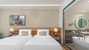 A hotel room with two beds, a large mirror, a bathtub, and a wall-mounted picture. - Taj Alibaug Resort & Spa (Alibag)