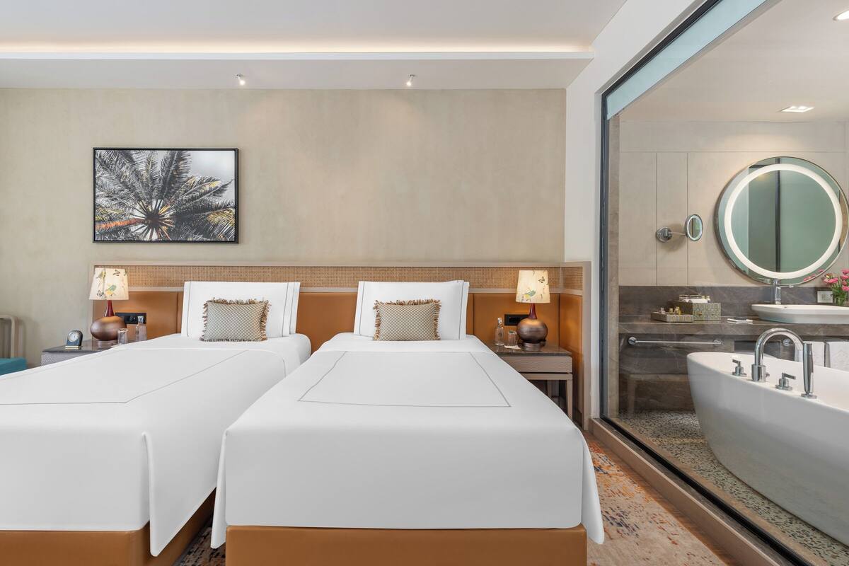 Habitación de hotel con dos camas, un espejo grande, una bañera e imagen colgada en la pared.