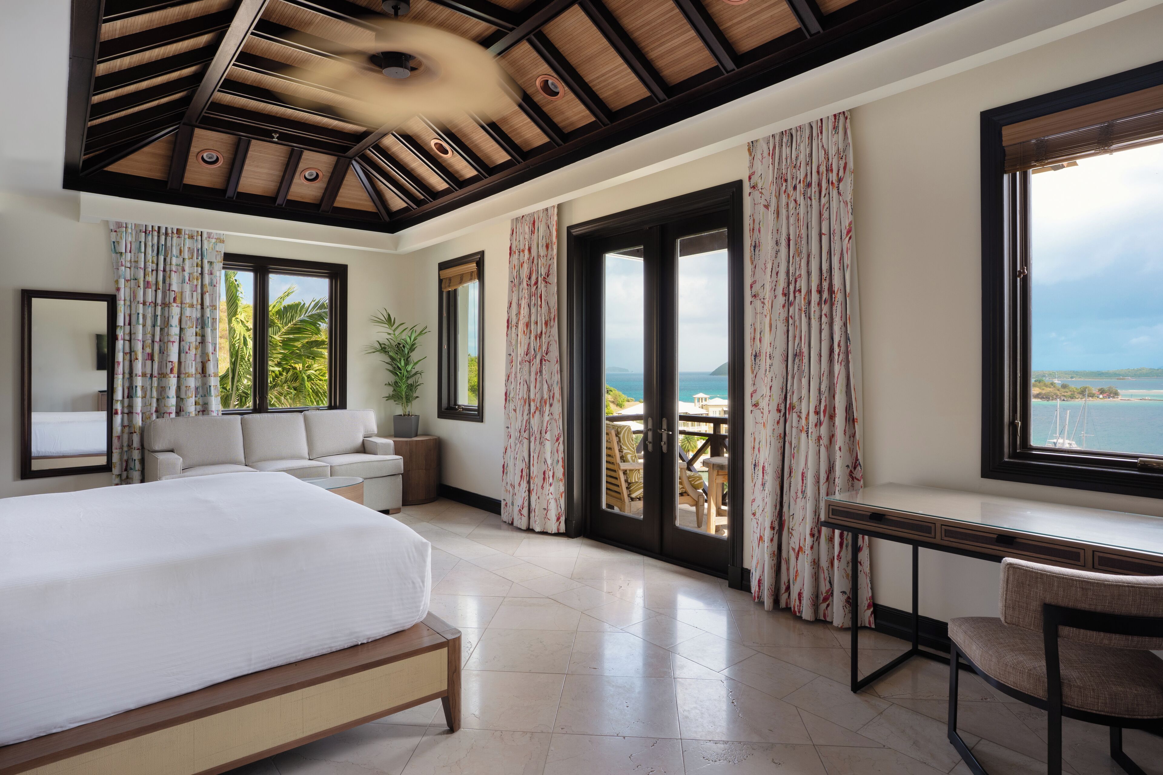 A spacious bedroom with a large bed, a desk, and a view of the sea.