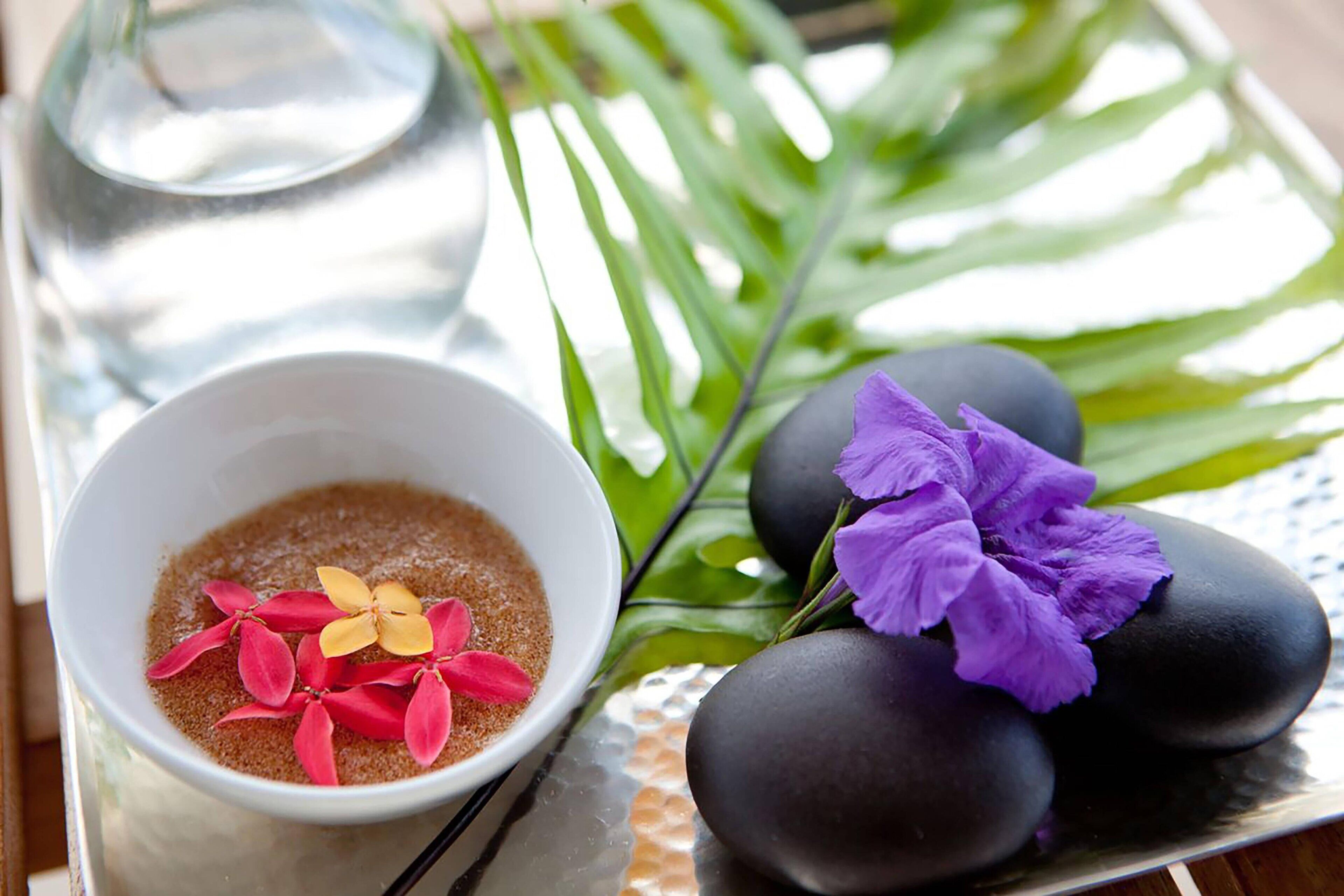 A bowl of brown sugar with red and yellow flowers, black stones, and a green leaf on a tray.