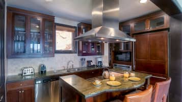A modern kitchen with a central island, stainless steel appliances, wooden cabinets, and a large window.