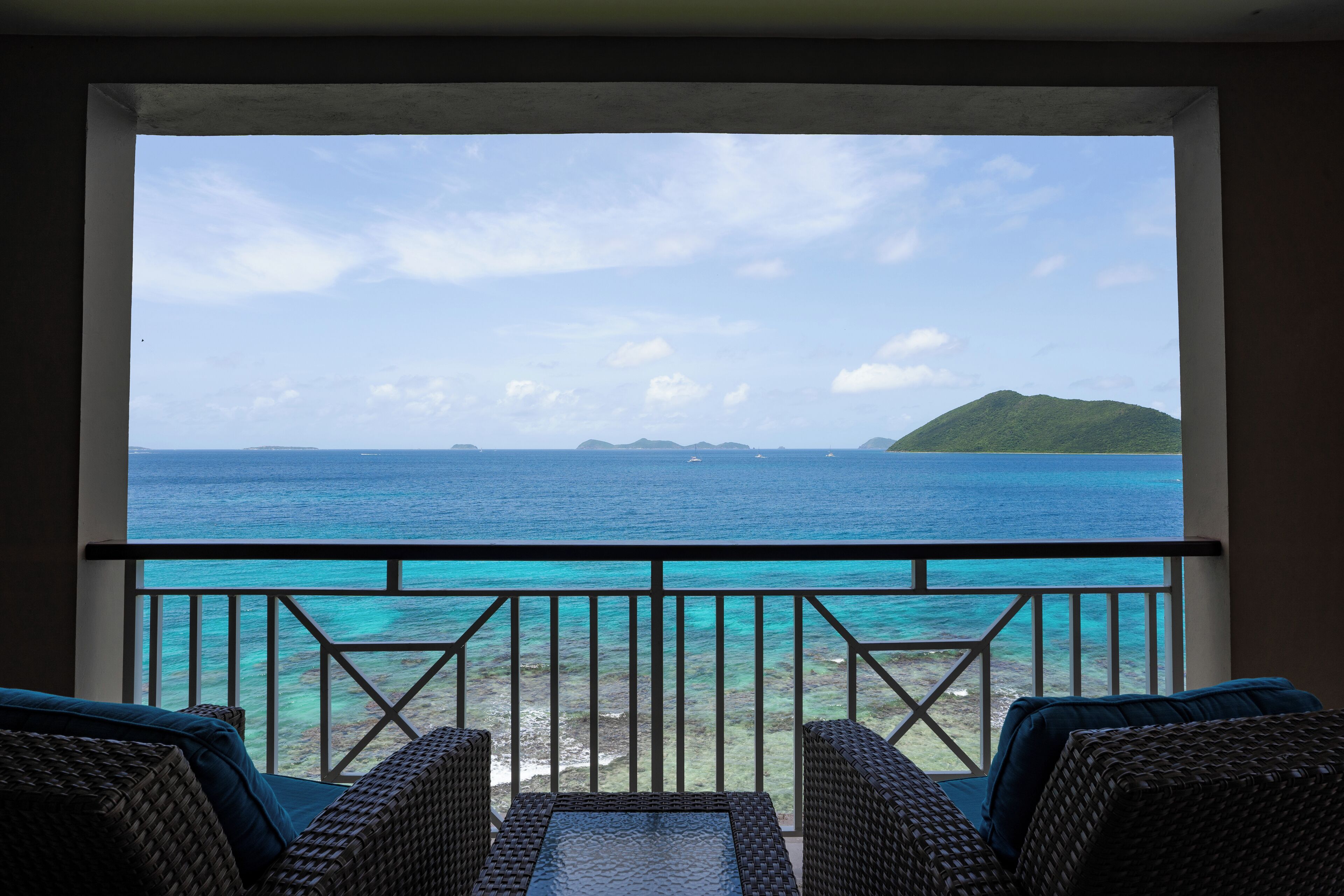 A balcony with wicker furniture overlooking a turquoise sea and distant islands.