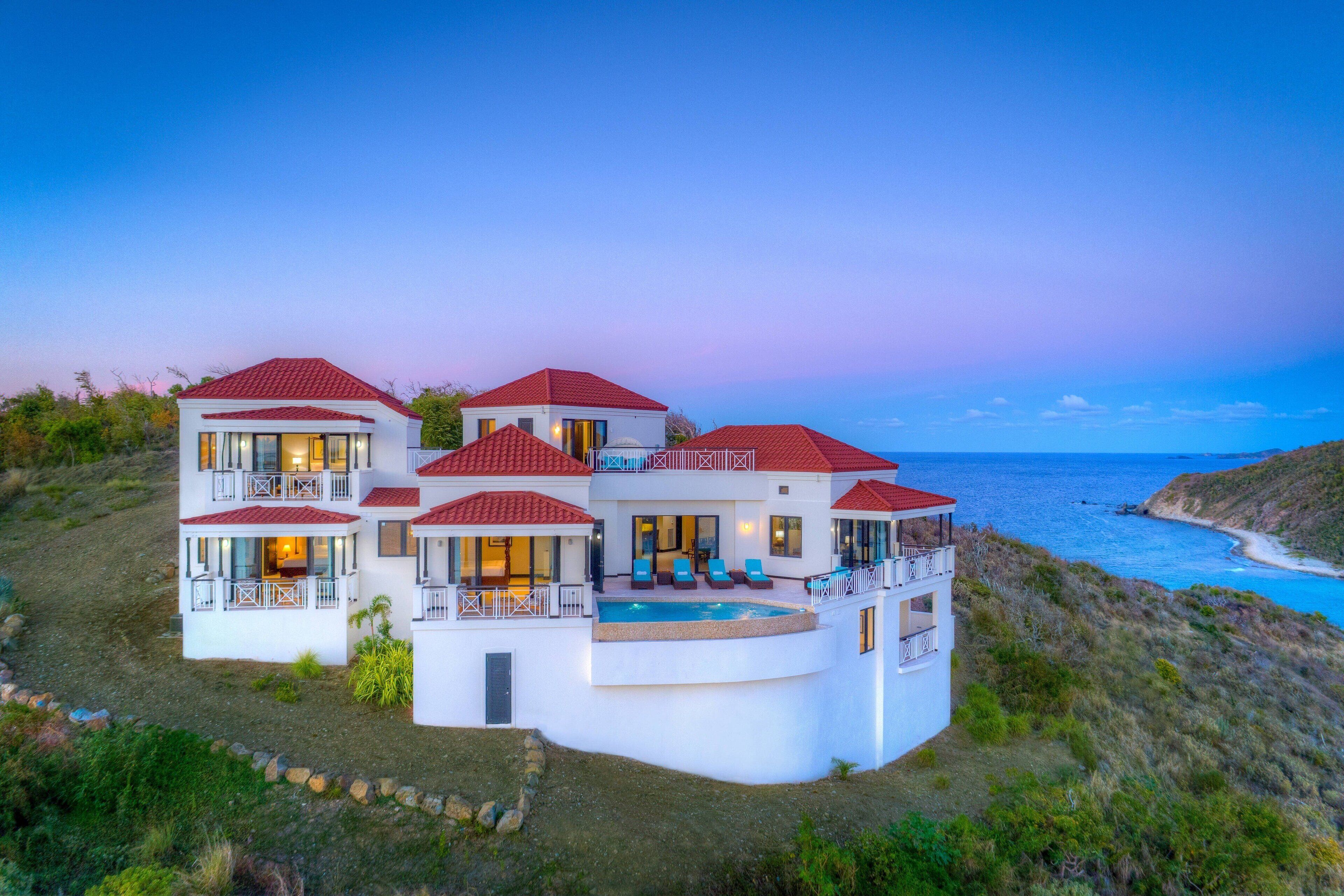 A large, multi-story house with a pool, located near a coastline.