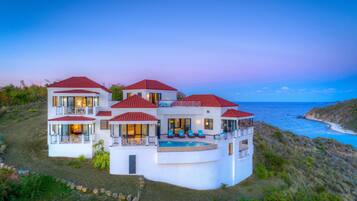A large, multi-story house with a pool, located near a coastline.
