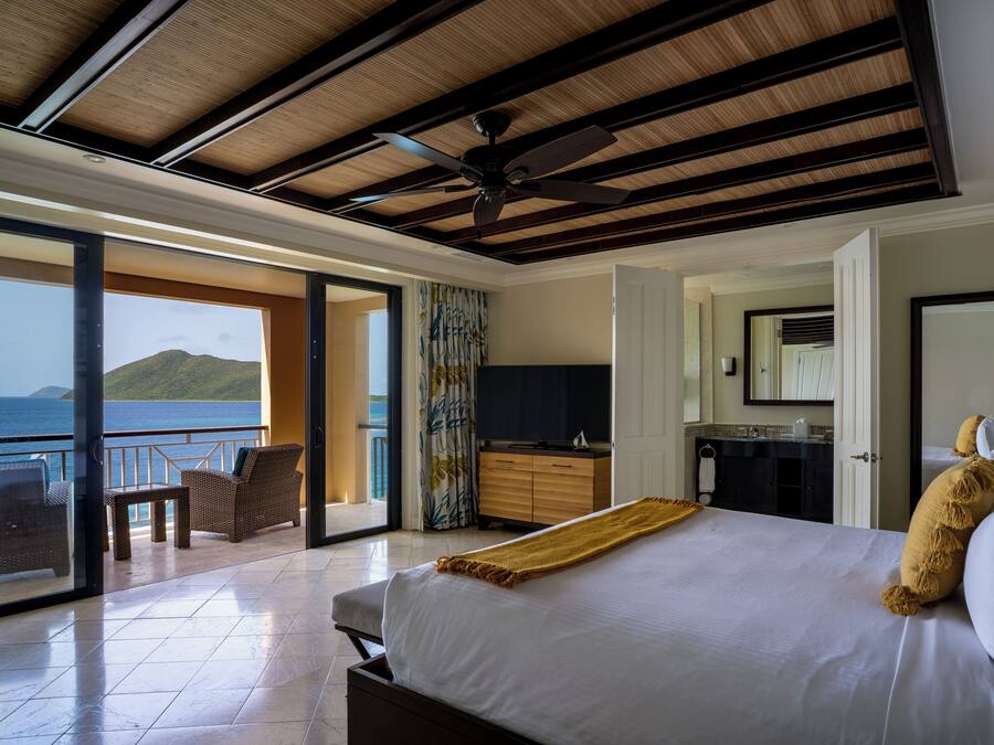 A hotel room with a balcony, a bed, a desk, and a view of the sea.