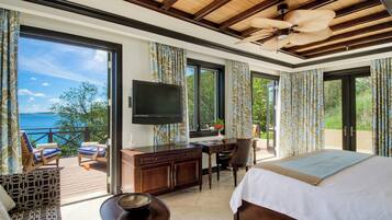 Een slaapkamer met een groot bed, een bureau, een televisie en een balkon met uitzicht op zee.