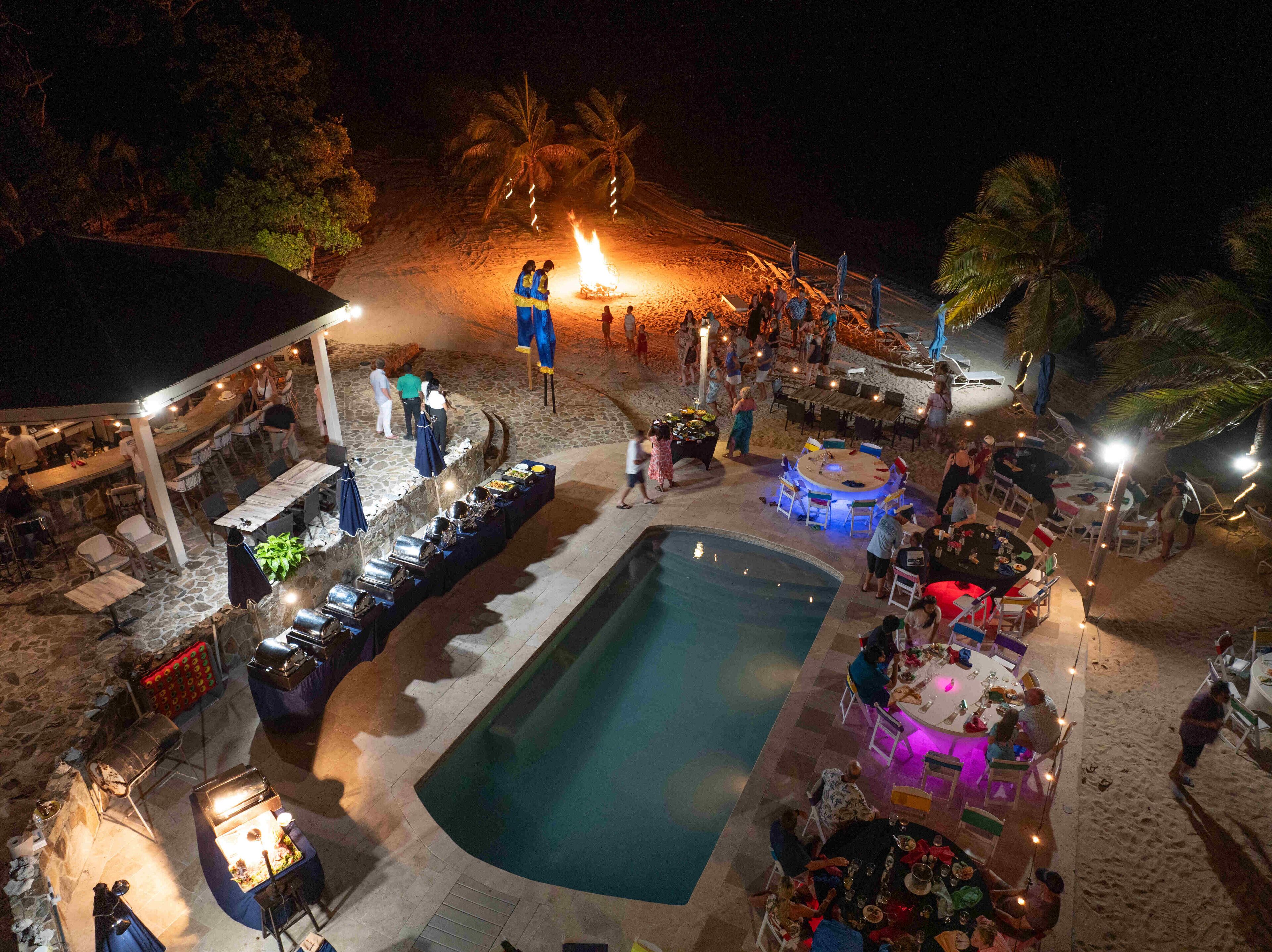 Un área de piscina al aire libre con bar y zona de comedor, rodeada de palmeras y un entorno playero.